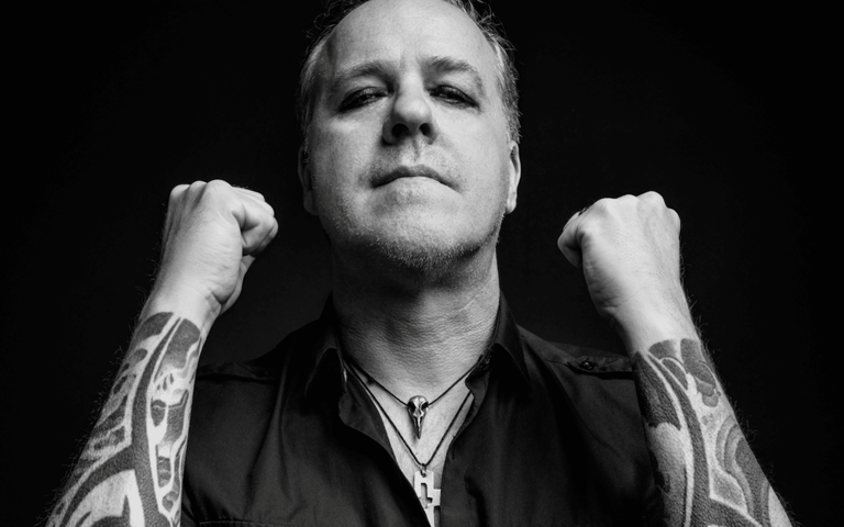 Tattooed performer with fists raised against a black background during a tour.