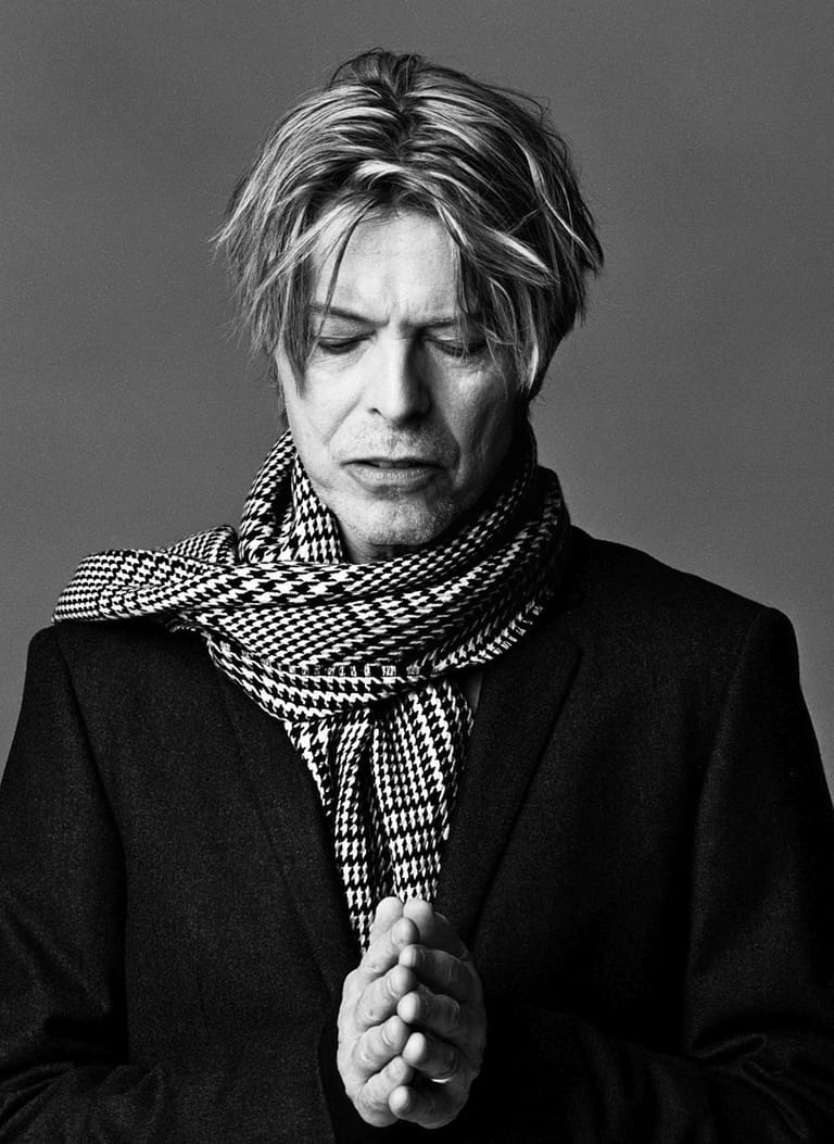 Person with layered dark hair wearing black jacket and checked scarf, gazing downward in monochrome portrait.