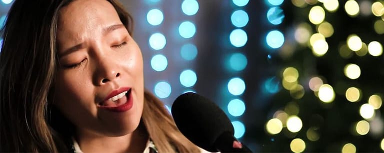Singer with red lipstick performing at microphone against bokeh-lit backdrop.