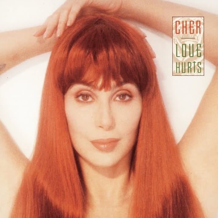Person with long, straight reddish-orange hair and full fringe, arms raised to head against a pale background.