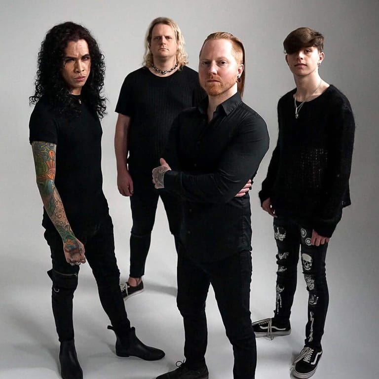 Four musicians in black clothing posed together against a neutral grey background.