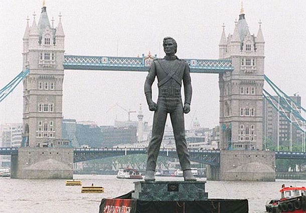 Bronze statue of a figure standing before Tower Bridge on the River Thames in London.