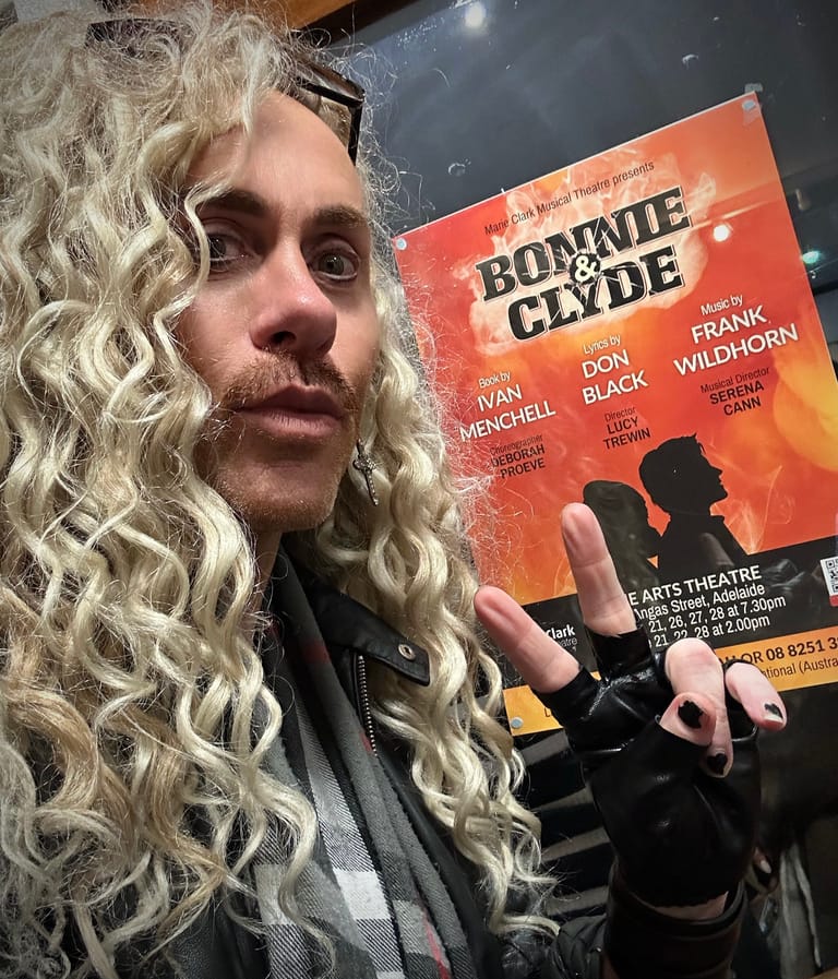 Person with long wavy hair holding a Bonnie & Clyde theatre poster featuring silhouetted figures against an orange background.