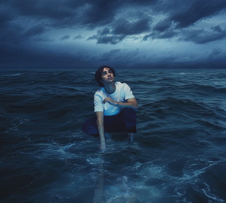 Person wading in stormy ocean waters under dark, brooding sky.