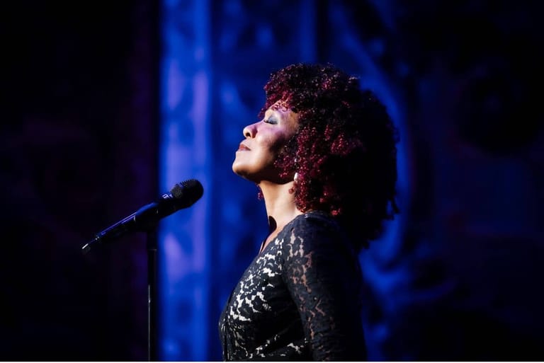Singer in a sequined jacket performs at a microphone bathed in blue stage lighting.