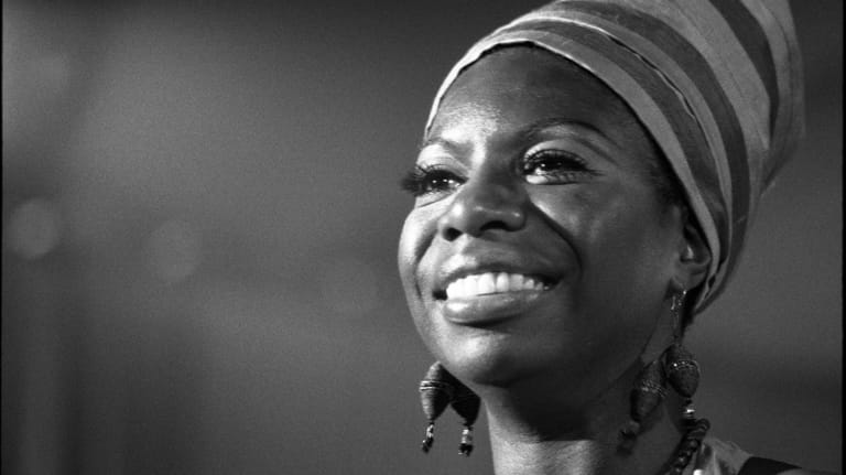 Woman in a striped headwrap smiling warmly against a dark background in black and white.