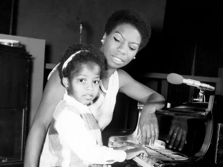 Woman and child seated at piano together in black and white archival photograph.