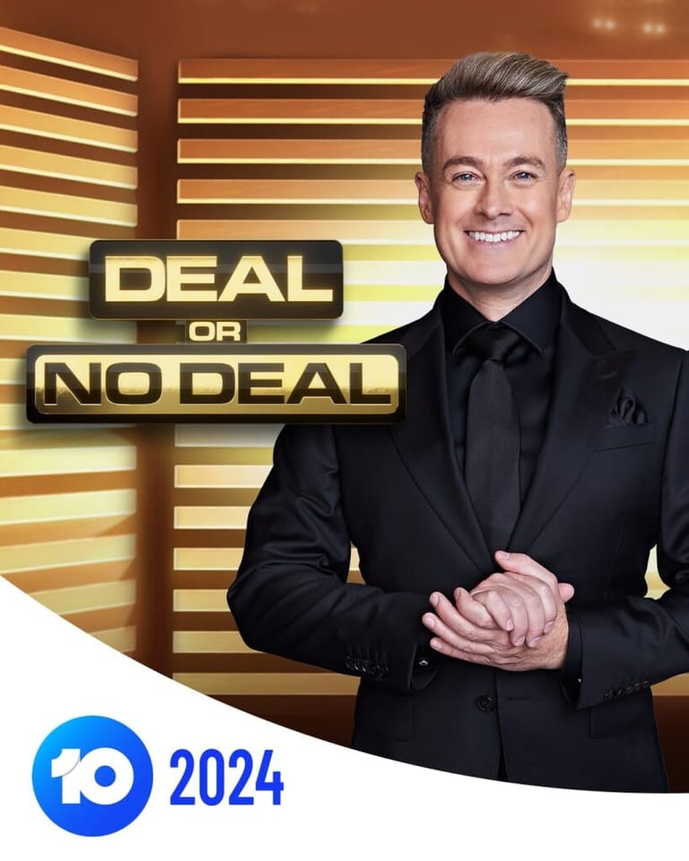 Man in black suit smiling before gold-striped backdrop with "Deal or No Deal" signage.