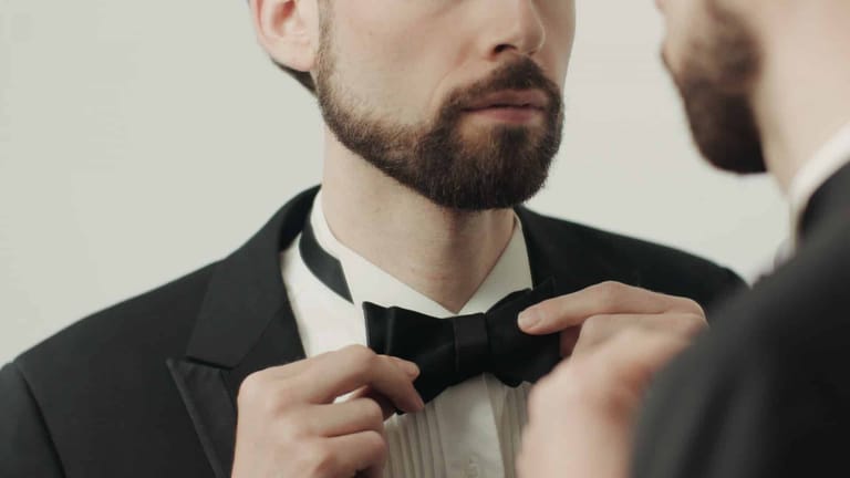 Man in formal attire adjusting his black bow tie before an event.