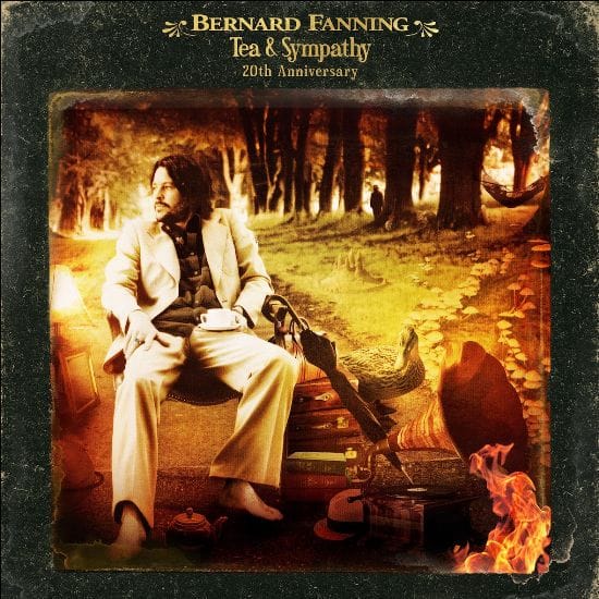 Musician seated by a campfire in an autumn forest wearing a cream suit and holding a guitar.