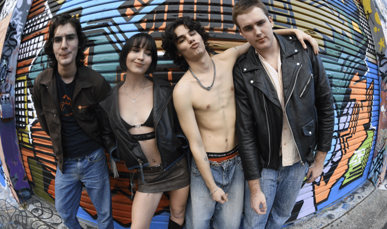Four band members pose against a colourful urban mural backdrop in casual leather and denim attire.