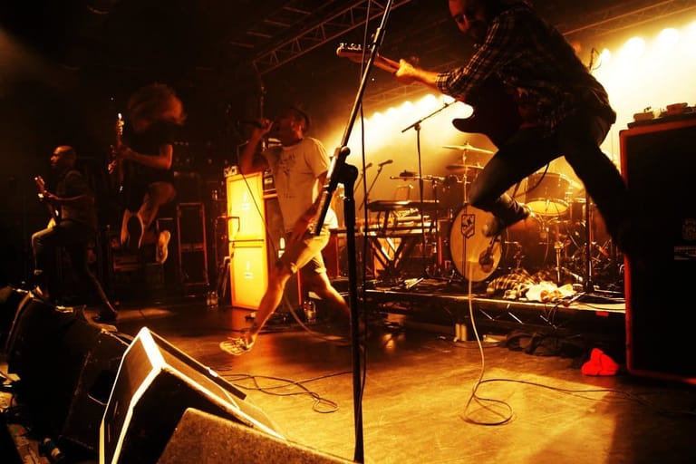 Band performing on an intimate venue stage bathed in warm golden lighting.