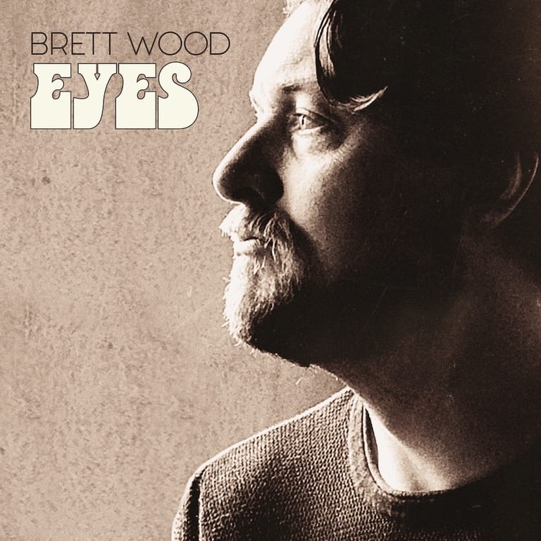 Bearded man in profile against a sepia-toned background, with "BRETT WOOD" and "EYES" text overlay.