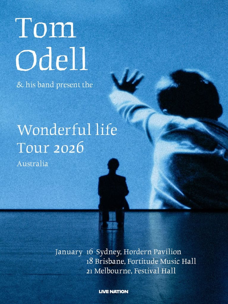 A silhouetted figure sits alone on stage beneath a large projected image of an outstretched hand against a blue backdrop.