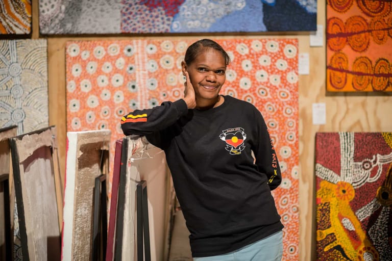 Person in black sweatshirt gestures toward patterned textiles displayed on studio walls.