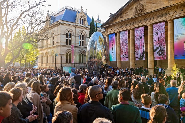 Large outdoor crowd gathered in front of an ornate heritage building with colourful banners displayed on its facade.