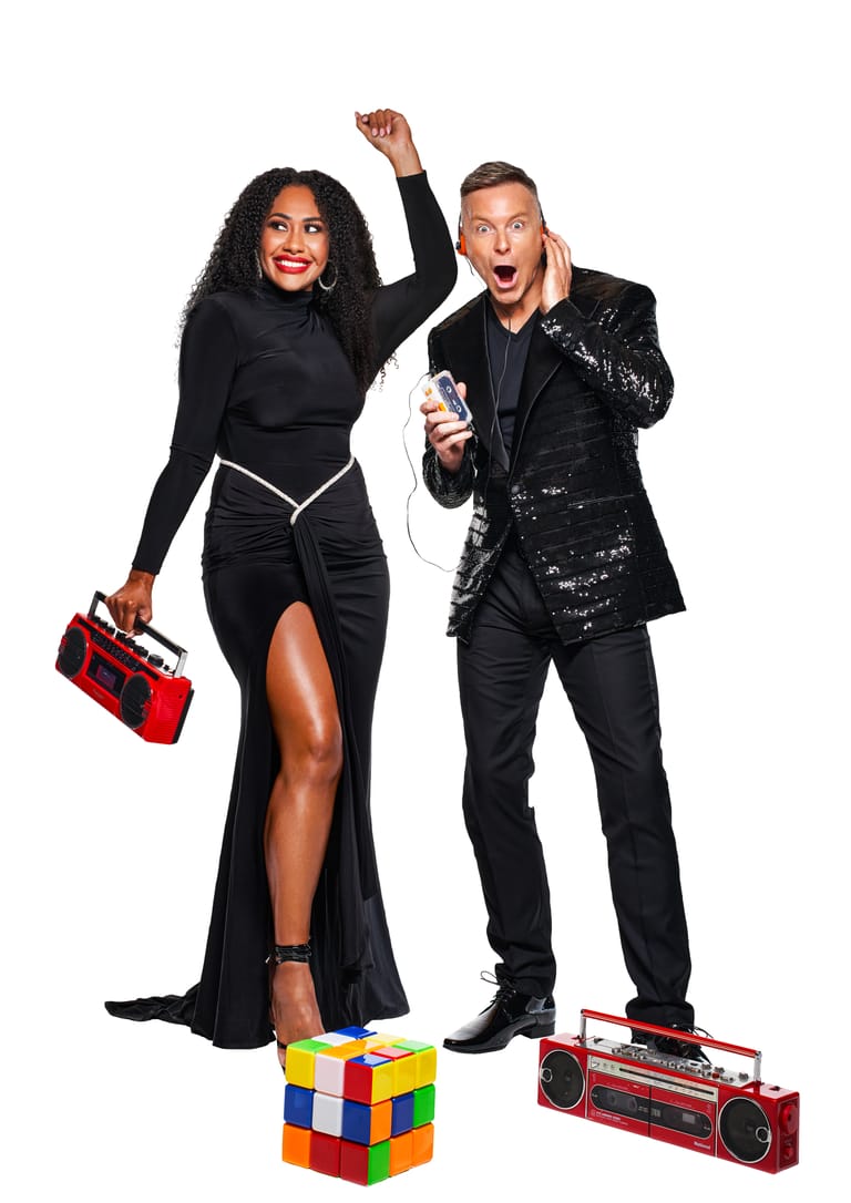 Two performers in black sequined outfits pose energetically with a Rubik's cube and boombox, ready for tour.