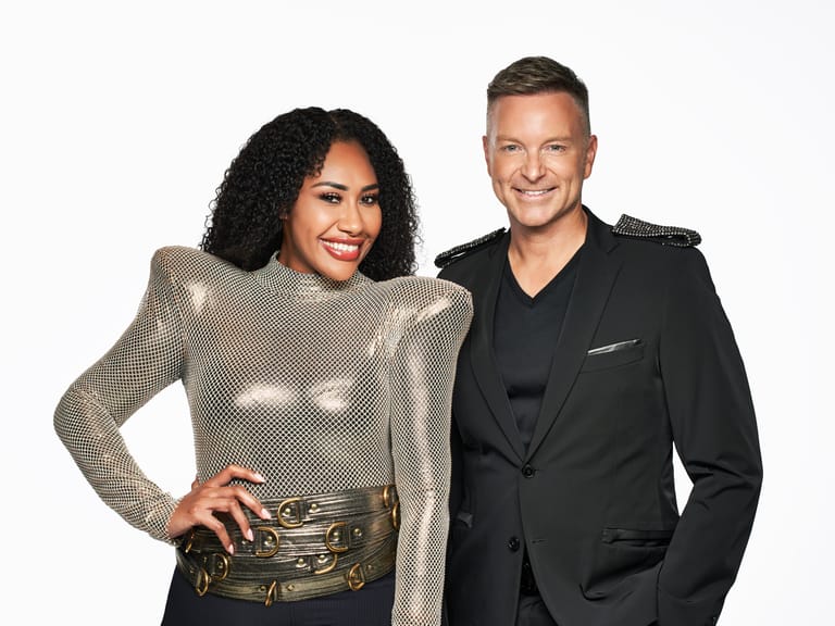 Two smiling people pose together against a white background, one wearing a shimmering gold top and the other in a black blazer.