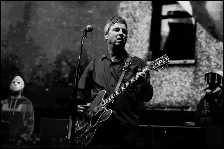 Musician performing with electric guitar at a microphone during a concert tour.