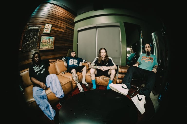 Four band members seated in a tour bus interior, relaxed and casual during downtime.