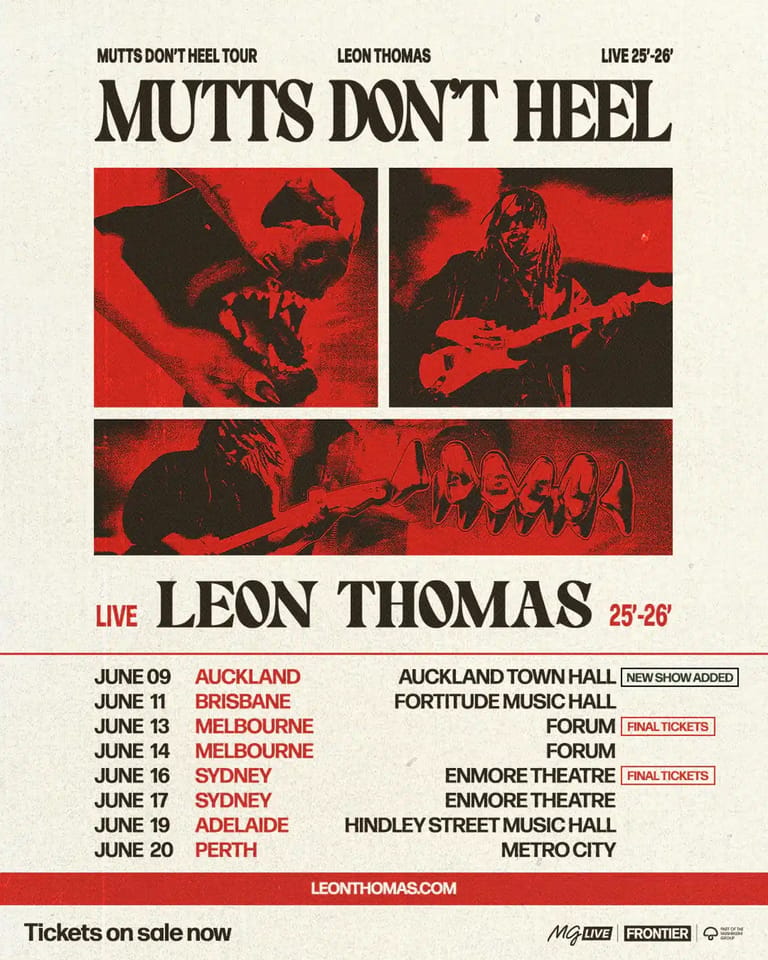 Musician Leon Thomas performing with guitar under red stage lighting during the Mutts Don't Heel tour.