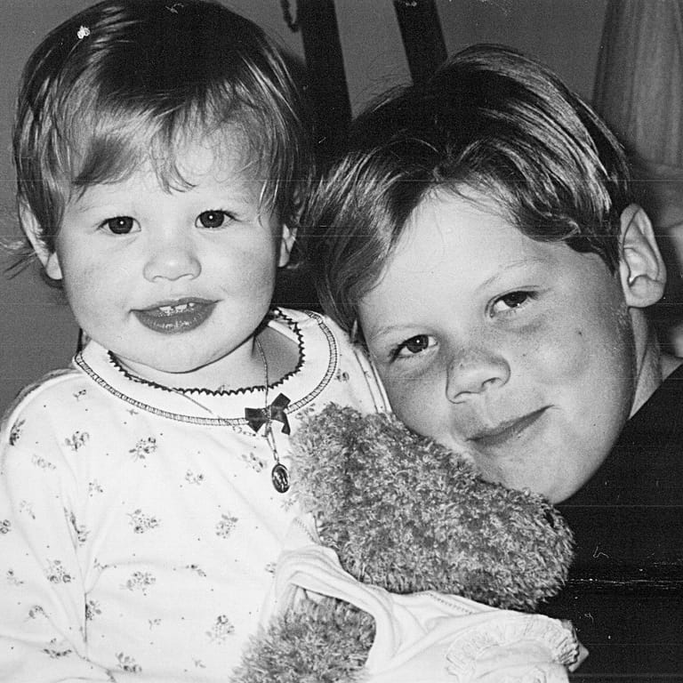 Two young children pose together in a black and white photograph, smiling at the camera.