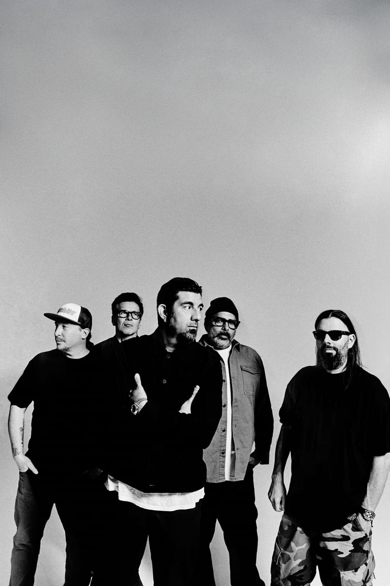 Five band members in dark clothing posed together against a plain grey background.