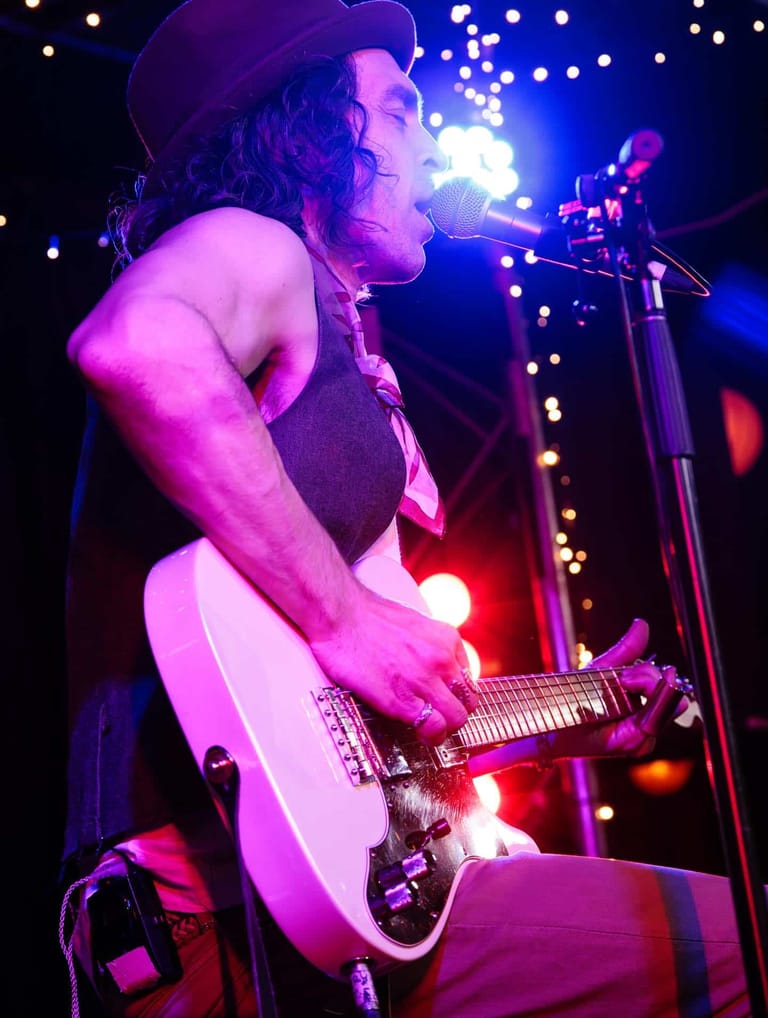 Guitarist performs at microphone under vibrant stage lighting during a concert tour.