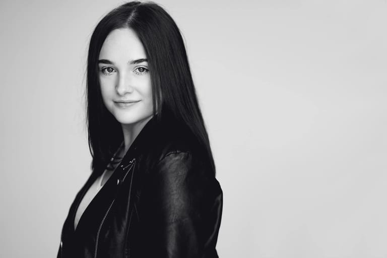 Woman with long dark hair in black leather jacket against neutral background.