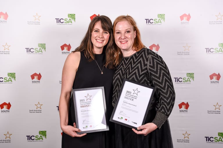 Two women hold awards at a TICSA ceremony, smiling at the camera against a branded backdrop.