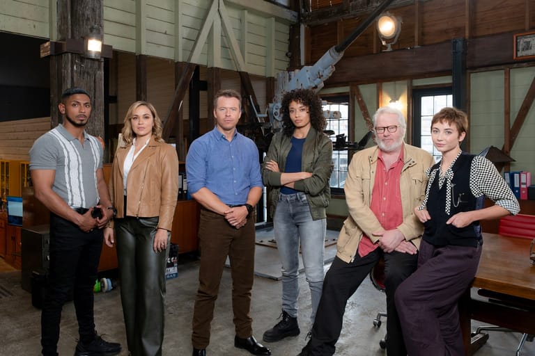 Six people stand together inside a rustic warehouse-style venue with exposed beams and industrial lighting.