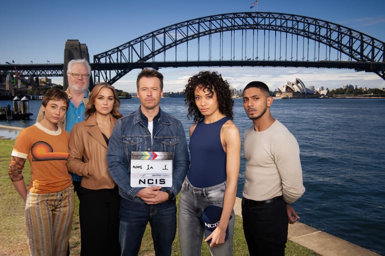 Cast members of NCIS: Sydney pose together at Circular Quay with the Harbour Bridge behind them.