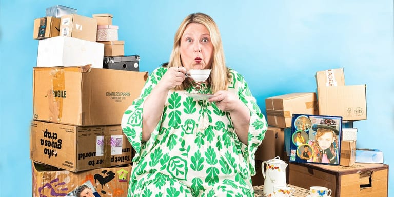 Person in green patterned dress surrounded by stacked cardboard boxes against bright blue background.