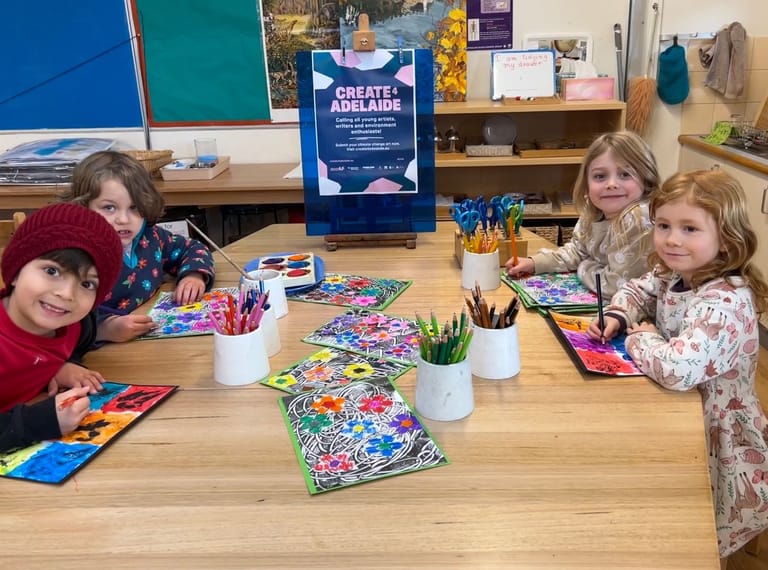 Four children seated at a wooden table colouring in artwork during a creative workshop or event.