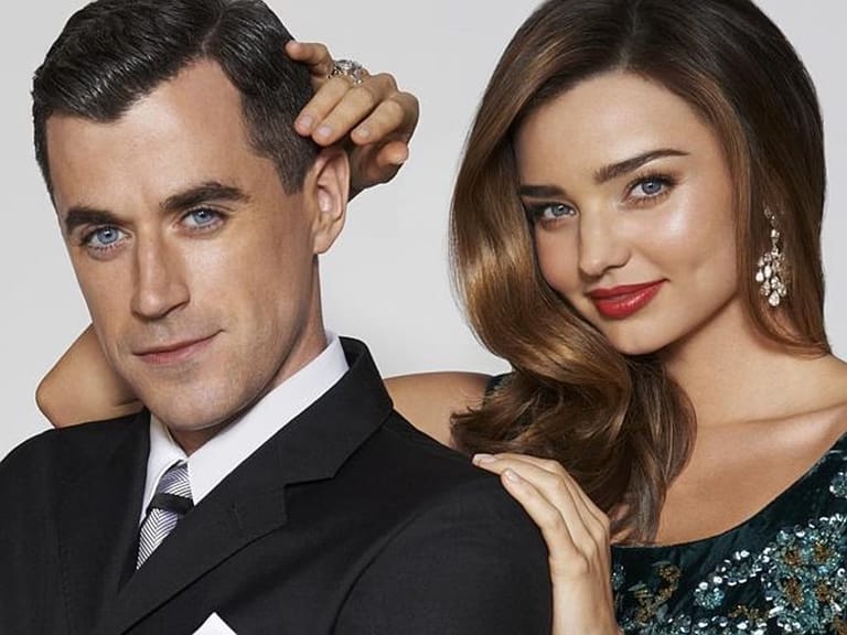 Two people pose together for a professional portrait against a neutral background.