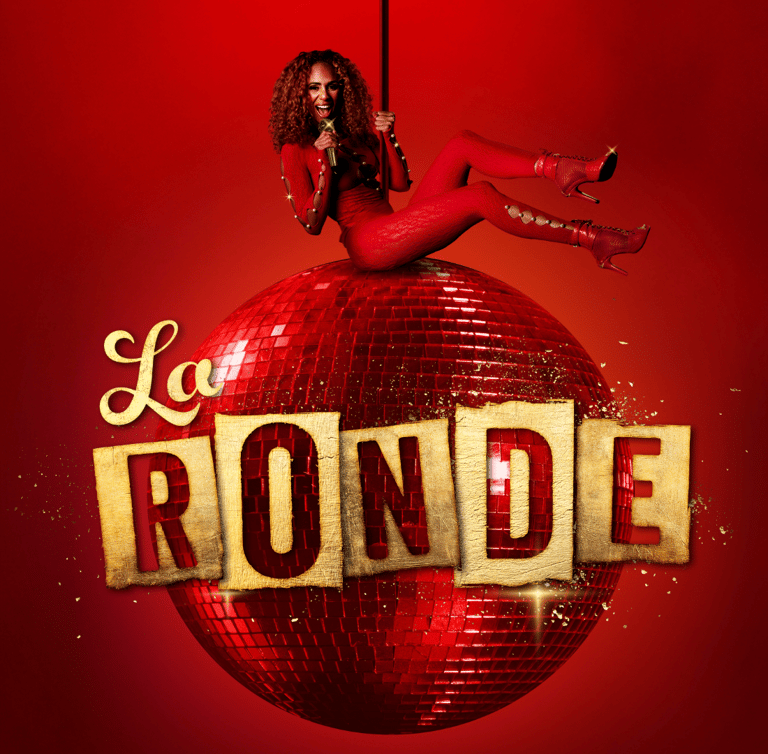 Performer perched atop a glittering red disco ball against a crimson background, holding a microphone.
