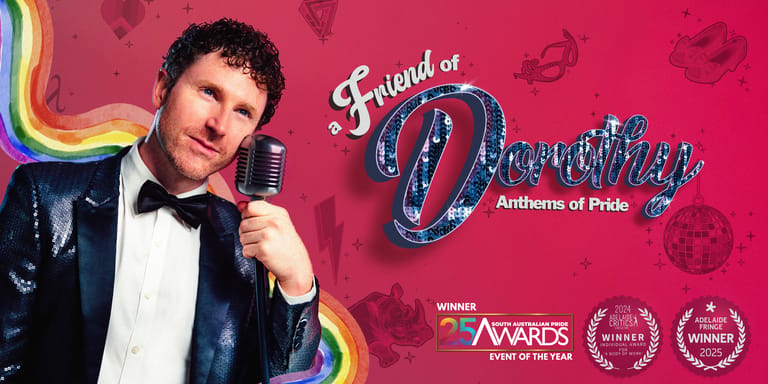 Man in black tuxedo jacket and bow tie holding microphone against pink backdrop with rainbow and award logos.