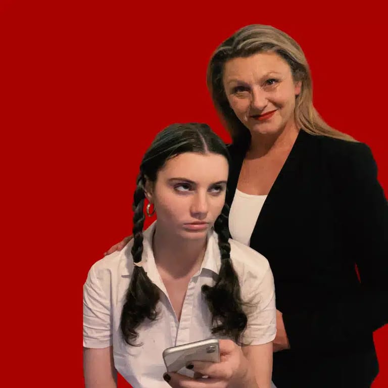 Two performers pose against a bright red background; one wears a white shirt with braided hair, the other a black blazer.