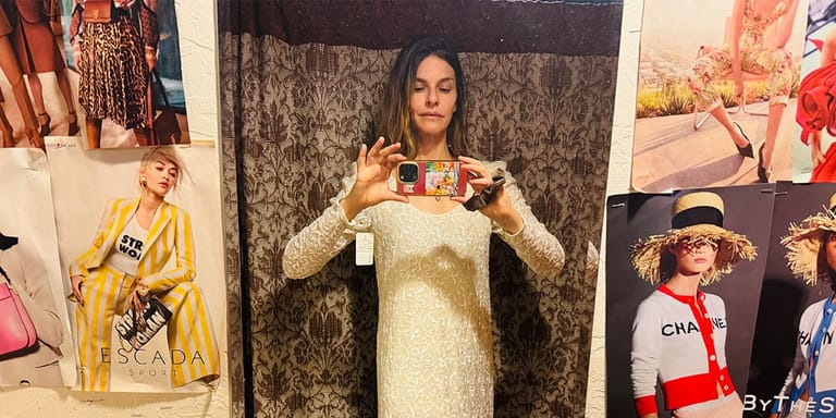 Performer in a pale green dress holding a framed photograph, surrounded by fashion imagery and vintage clothing displays.