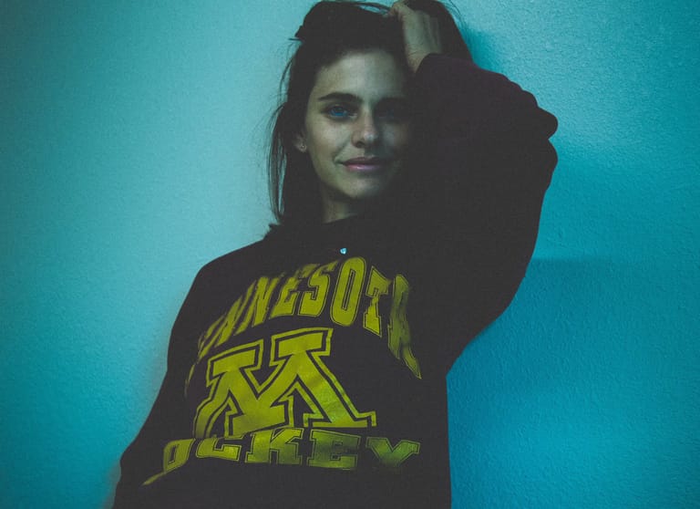 Person wearing a dark hoodie with yellow lettering against a blue-tinted background.