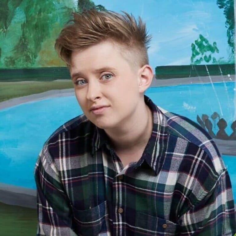 Young person in a navy and green tartan shirt posing against a colourful mural backdrop featuring a swimming pool.