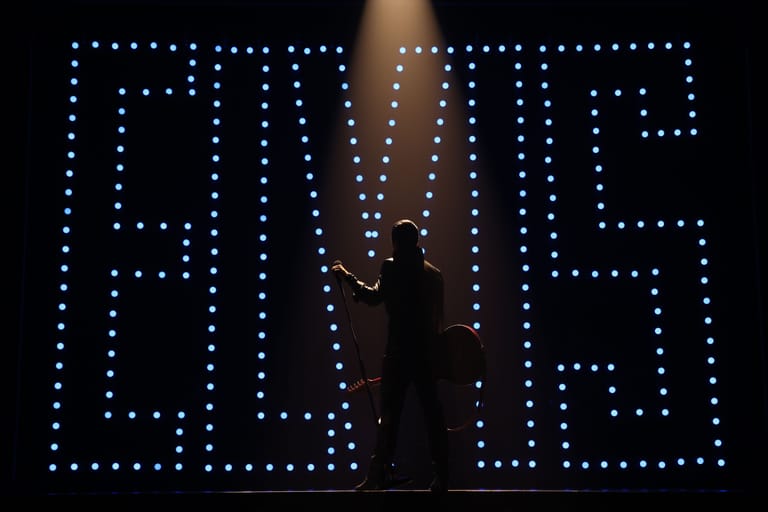 Silhouetted figure ascending a rope against an illuminated LED backdrop spelling "LOVE".