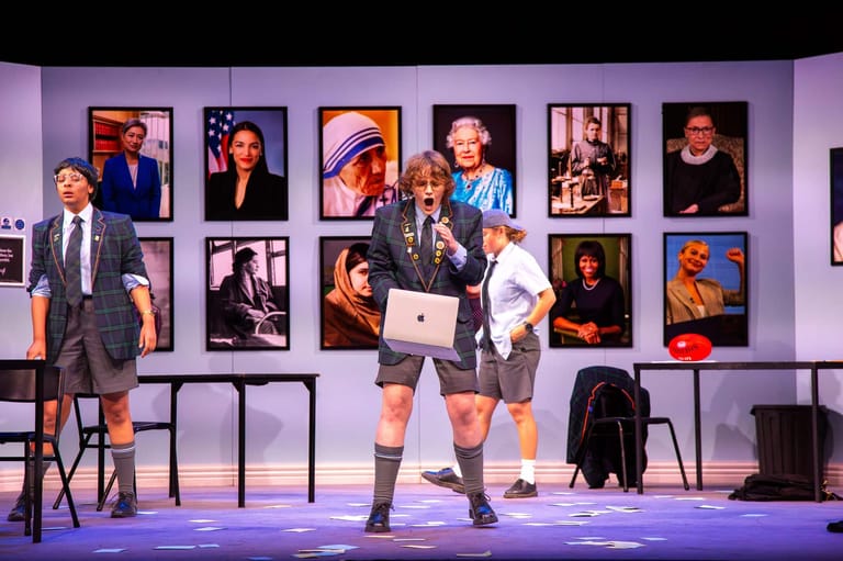 Two performers on stage with portrait photographs displayed on the wall behind them during a State Theatre Company South Australia production.