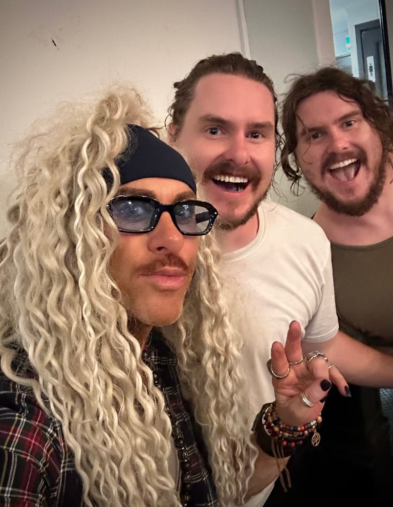 Three people pose together indoors, smiling at the camera in a candid group photo.
