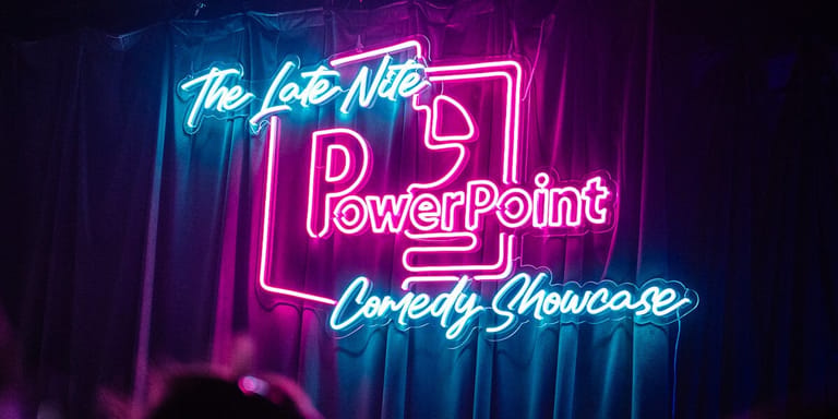 Neon signs reading "The Late Nite PowerPoint Comedy Showcase" glow in pink and blue against a dark curtained backdrop.