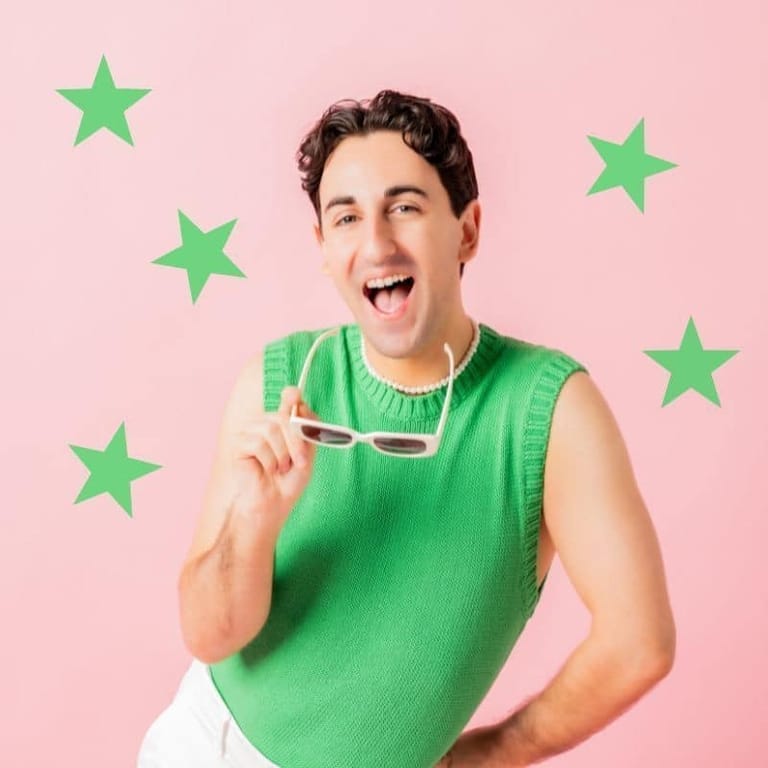 Man in bright green sleeveless shirt holding sunglasses against pink background with green stars.