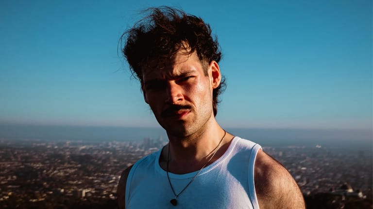 Man in white sleeveless shirt overlooking sprawling cityscape under clear blue sky.