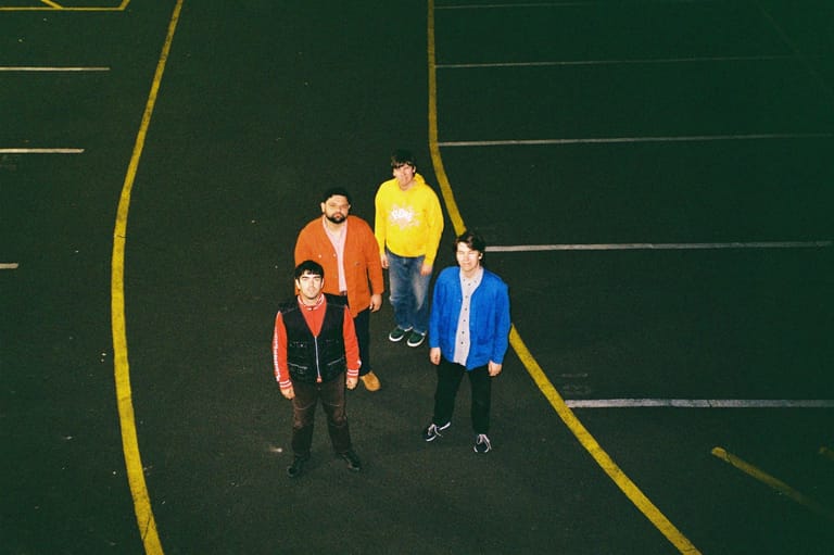 Four people in high-visibility jackets stand on a green sports court marked with yellow lines.