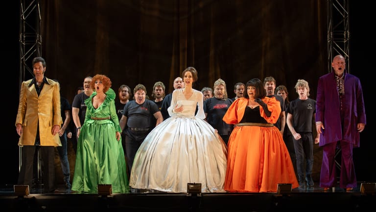 Cast members in colourful period costumes stand on stage during a theatrical production of Cinderella.