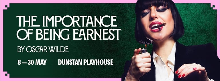 Woman in black and white outfit with dark fringe smiles against green background promoting Wilde's theatrical comedy.